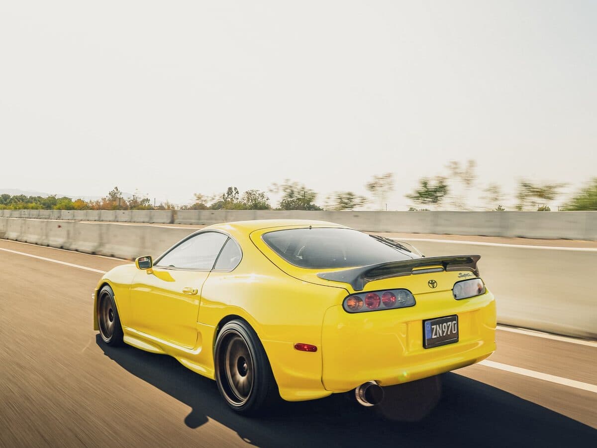A yellow Japanese sports coupé accelerating along a highway
